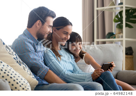 Family with kid daughter smiling looking at smartphone making vi Family with kid daughter smiling looking at smartphone making vi 64982148