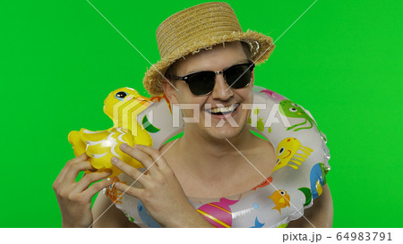 Shirtless young man tourist with swimming ring on shoulders plays with duck toy Shirtless young man tourist with swimming ring on shoulders plays with duck toy 64983791