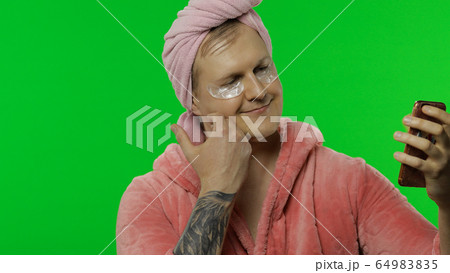Portrait of transsexual man in bathrobe making selfies using mobile phone 64983835