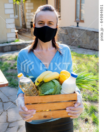 A woman in a protective medical mask with a food kit in a wicker basket for the poor. 64984601