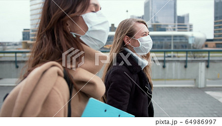 Epidemic control social workers. Two young Caucasian female doctors in face masks walk on city street during quarantine. 64986997