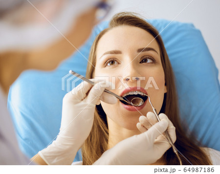 Smiling young woman with orthodontic brackets examined by dentist at dental clinic 64987186