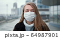 Epidemic quarantine. Portrait of young Caucasian woman wearing mask outdoors, turning head to camera in empty street. 64987901