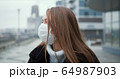 Epidemic quarantine. Portrait of young Caucasian woman wearing mask outdoors, turning head to camera in empty street. 64987903