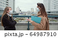Epidemic control social care workers. Two young Caucasian female social care employees in face masks talk outside. 64987910