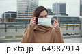 COVID-19 epidemic protection, danger and fear atmosphere. Portrait of beautiful Caucasian woman putting mask on outside. 64987914