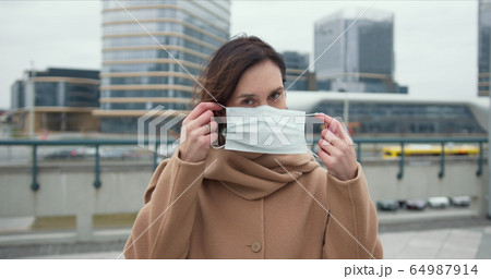 COVID-19 epidemic protection, danger and fear atmosphere. Portrait of beautiful Caucasian woman putting mask on outside. 64987914