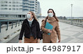 Two young doctor women wear masks walking in empty windy city street. Fear and danger atmosphere on epidemic quarantine. 64987917