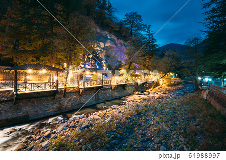 Borjomi, Georgia. Night View Of Borjomula Mountain River Passing Through City, Park And Street Gazebo. Landscape Of Rocky River At Evening Night Illumination. 64988997