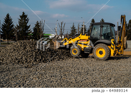 Yellow wheel loader Excavator machine working at construction site with gravel. Preparing of the fundament for a asphalting. Road construction site. Building of a parking. Yellow wheel loader Excavator machine working at construction site with gravel. Preparing of the fundament for a asphalting. Road construction site. Building of a parking. 64989314