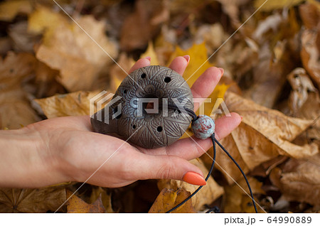 Female hand with orange manicure holds ceramic ocarina in the forest during autumn. Relaxing tranquil scene, traditional music concepts 64990889