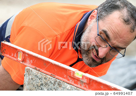 Construction worker checking the bubble level while working at construction site. Building Construction worker checking the bubble level while working at construction site. Building 64991407
