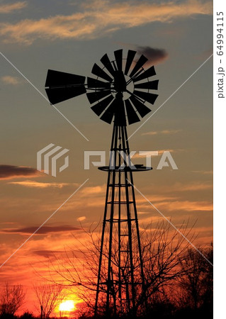 Kansas colorful Sunset with a Windmill silhouette with clouds and tree's and the Sun. Kansas colorful Sunset with a Windmill silhouette with clouds and tree's and the Sun. 64994115