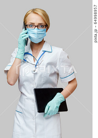 medical doctor nurse woman wearing protective mask and gloves - holding tablet pc and mobile phone medical doctor nurse woman wearing protective mask and gloves - holding tablet pc and mobile phone 64998957
