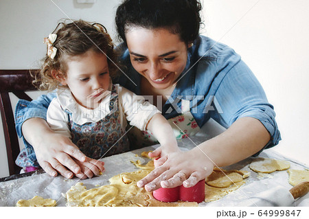 Mother and daughter baking cookies in the kitchen - cutting pastry dough with plastic shape cutters 64999847