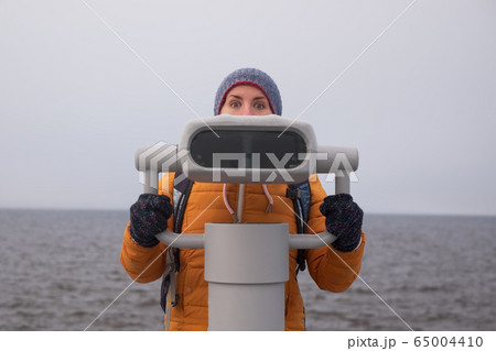 Young woman looking through a coin operated 65004410