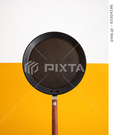 Flat metallic pancake pan with brown wooden handle on yellow and white background with copy space. Flat metallic pancake pan with brown wooden handle on yellow and white background with copy space. 65004596
