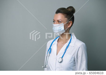 A female doctor in a white robe and mask with a stethoscope. 65004610