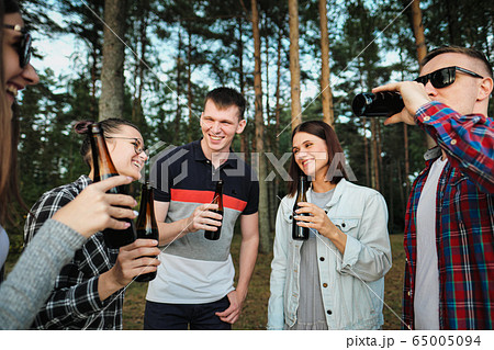 A group of friends rests and relaxes in nature. People eat hamburgers, drink beer, communicate and laugh. A group of friends rests and relaxes in nature. People eat hamburgers, drink beer, communicate and laugh. 65005094