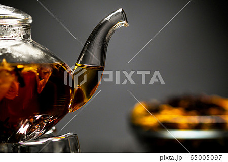 Horizontal photo of the tea set on a black background. Glass transparent teapot and cup. Black leaf tea. 65005097
