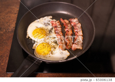 Frying pan with fried eggs and bacon on electric stove in process of cooking Frying pan with fried eggs and bacon on electric stove in process of cooking 65006138