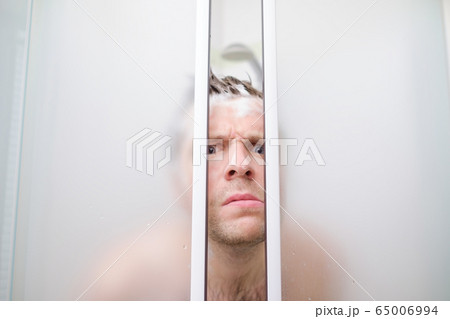 A young caucasian man peeks out of shower in soap. A young caucasian man peeks out of shower in soap. 65006994