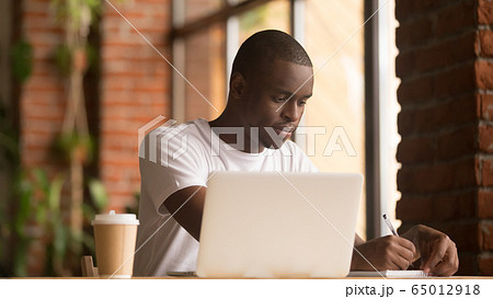 Serious african american man working studying with laptop making notes Serious african american man working studying with laptop making notes 65012918