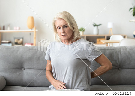 Worried sad older woman touching back feeling back pain Worried sad older woman touching back feeling back pain 65013114
