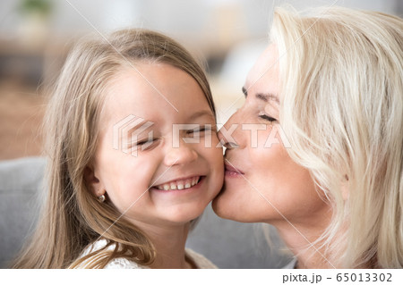 Loving old grandmother kissing cute preschool granddaughter on c 65013302