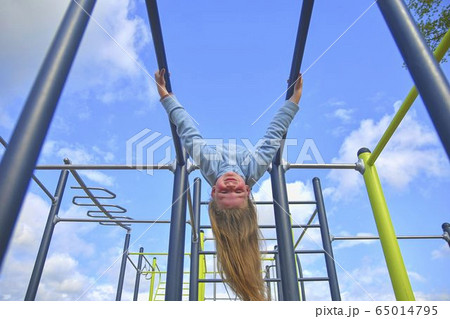 Little girl hanging upside down on parallel bars at playground. 65014795