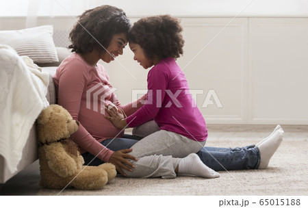 Happy Pregnant Black Woman And Her Cute Daughter Bonding At Home 65015188