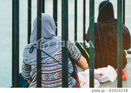 Back view of Muslim women relax and admire the beautiful scenery in the evening on The Bridge of the River Kwai in Kanchanaburi, Thailand. Back view of Muslim women relax and admire the beautiful scenery in the evening on The Bridge of the River Kwai in Kanchanaburi, Thailand. 65024238