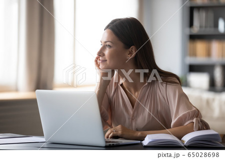 Dreamy young woman pondering ideas, sitting at desk with laptop 65028698