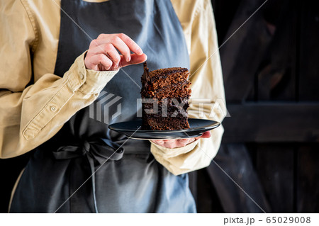 Pastry chef in apron holds chocolate cake 65029008