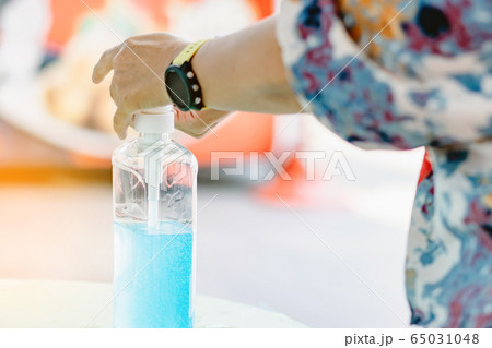 Woman uses her hand to press hand sanitizer bottle to clean her hand at wayside in the city. Concepts of Flu virus, Covid-19 (Coronavirus disease). Selective focus on alcohol gel bottle. 65031048