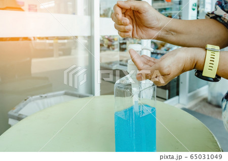 Woman uses her hand to press hand sanitizer bottle to clean her hand at wayside in the city. Concepts of Flu virus, Covid-19 (Coronavirus disease). Selective focus on alcohol gel bottle. 65031049