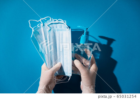 Woman hands in latex gloves holding facial medical masks and sanitizer, blue background Woman hands in latex gloves holding facial medical masks and sanitizer, blue background 65031254