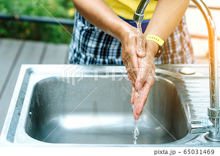 A woman washing hands from the tap with pink soap in a aluminium tub. Concepts of Flu virus, Covid-19 (Coronavirus disease). Selective focus. A woman washing hands from the tap with pink soap in a aluminium tub. Concepts of Flu virus, Covid-19 (Coronavirus disease). Selective focus. 65031469