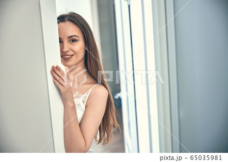 Caucasian smiling girl hiding behind the door at home Caucasian smiling girl hiding behind the door at home 65035981