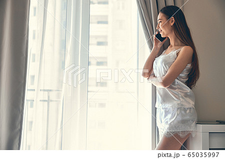 Caucasian slim girl standing near window and talking on phone 65035997