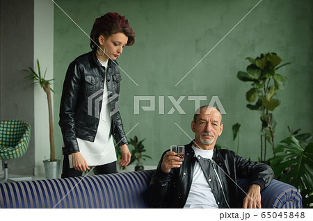 Indoor family portrait of adult daughter and senior father in loft style room with houseplants. Man is drunk with glass of whisky or brandy. Alcohol addiction concept Indoor family portrait of adult daughter and senior father in loft style room with houseplants. Man is drunk with glass of whisky or brandy. Alcohol addiction concept 65045848