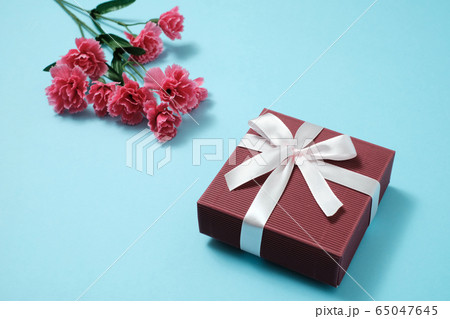 水色背景のリボンのついたプレゼントボックスとピンクのカーネーション 65047645