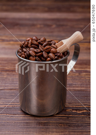 Brown coffee beans in a steel mug with wooden scoop. 65047690