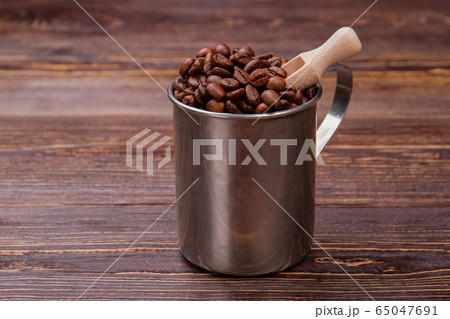 Short wooden scoop into steel mug with coffee beans. 65047691