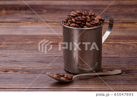Steel mug and teaspoon filled with coffee beans. 65047693