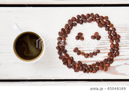 Top view cup of hot coffee and beans in a shape of smiley face. Top view cup of hot coffee and beans in a shape of smiley face. 65048169