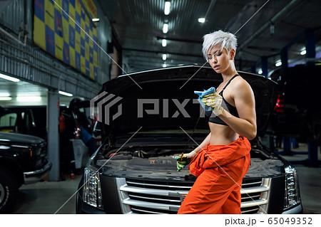 Girl mechanic checks engine oil. Scheduled oil change in the car. Car service. Girl mechanic checks engine oil. Scheduled oil change in the car. Car service. 65049352