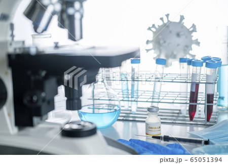 Microscope in laboratory with model of coronavirus, vials, and vaccine 65051394