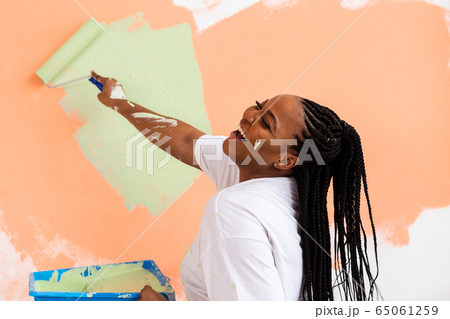 Afro woman painting the walls of new home. Renovation, repair and redecoration concept. Afro woman painting the walls of new home. Renovation, repair and redecoration concept. 65061259