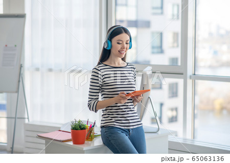 Dark-haired woman in headphones holding a tablet and watching something Dark-haired woman in headphones holding a tablet and watching something 65063136